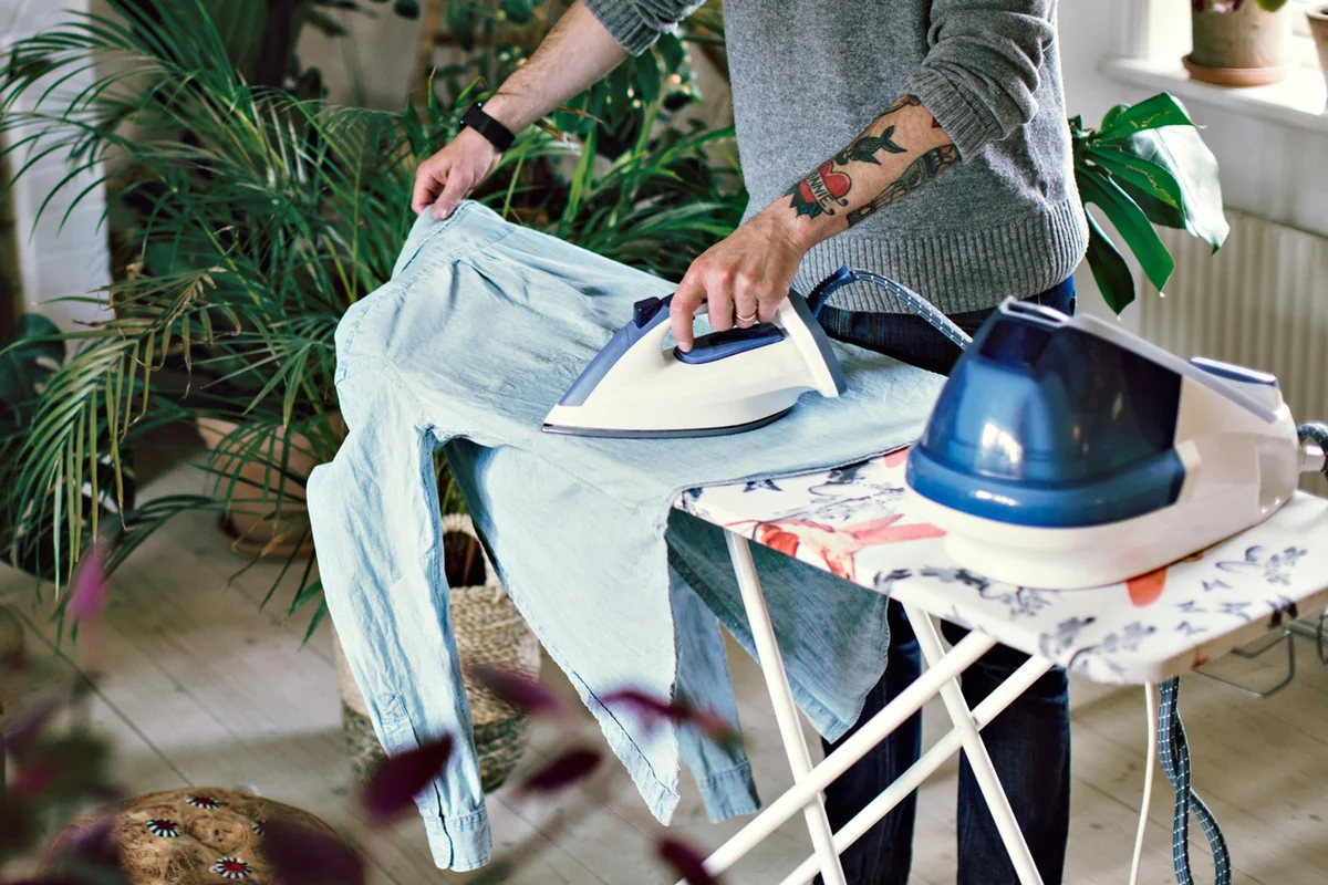 Man ironing his shirt on board in room at home