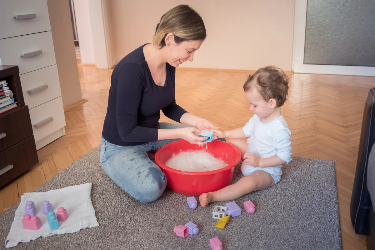 Mother and son playfully washing toys together in a living room