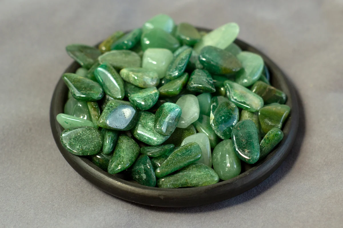 Natural mineral rock specimen, tumbled green aventurine gemstone on black plate