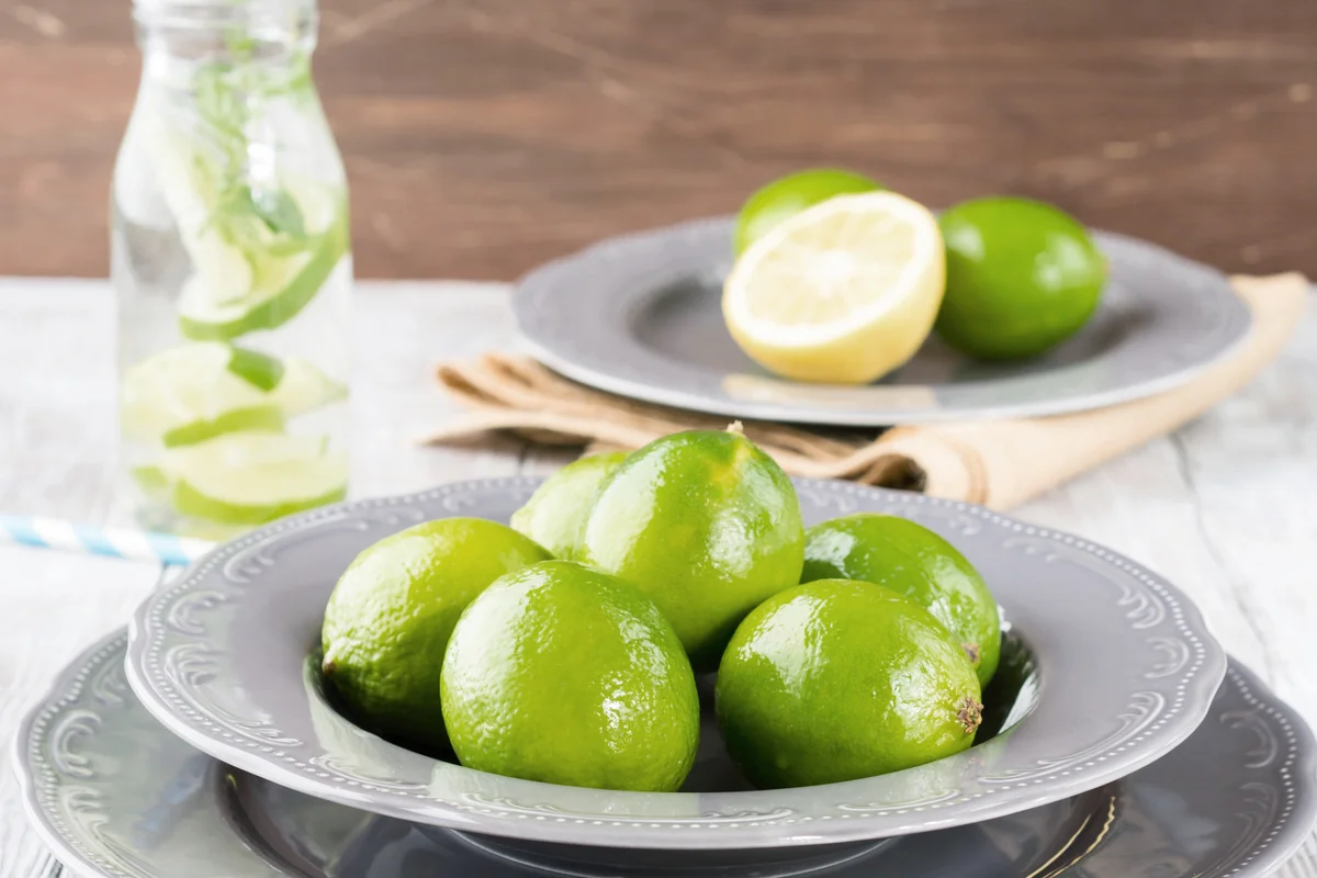 Fresh green limes on a plate with infused vodka in the background
