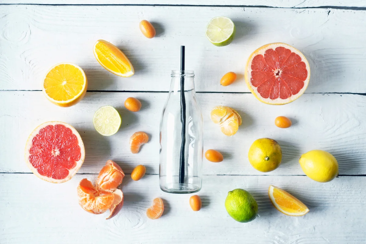 Glass bottle surrounded by different citrus on white wooden table