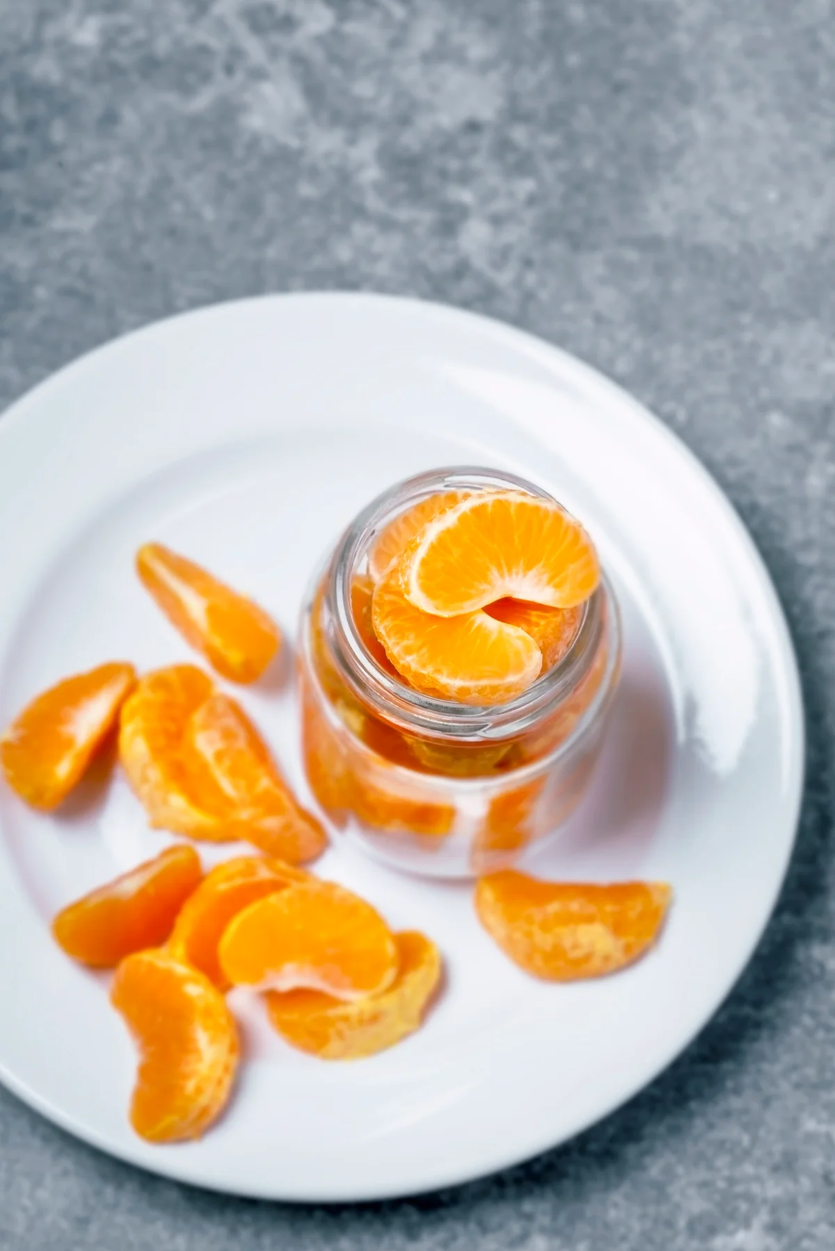 Peeled clementines segments on a jar and white plate