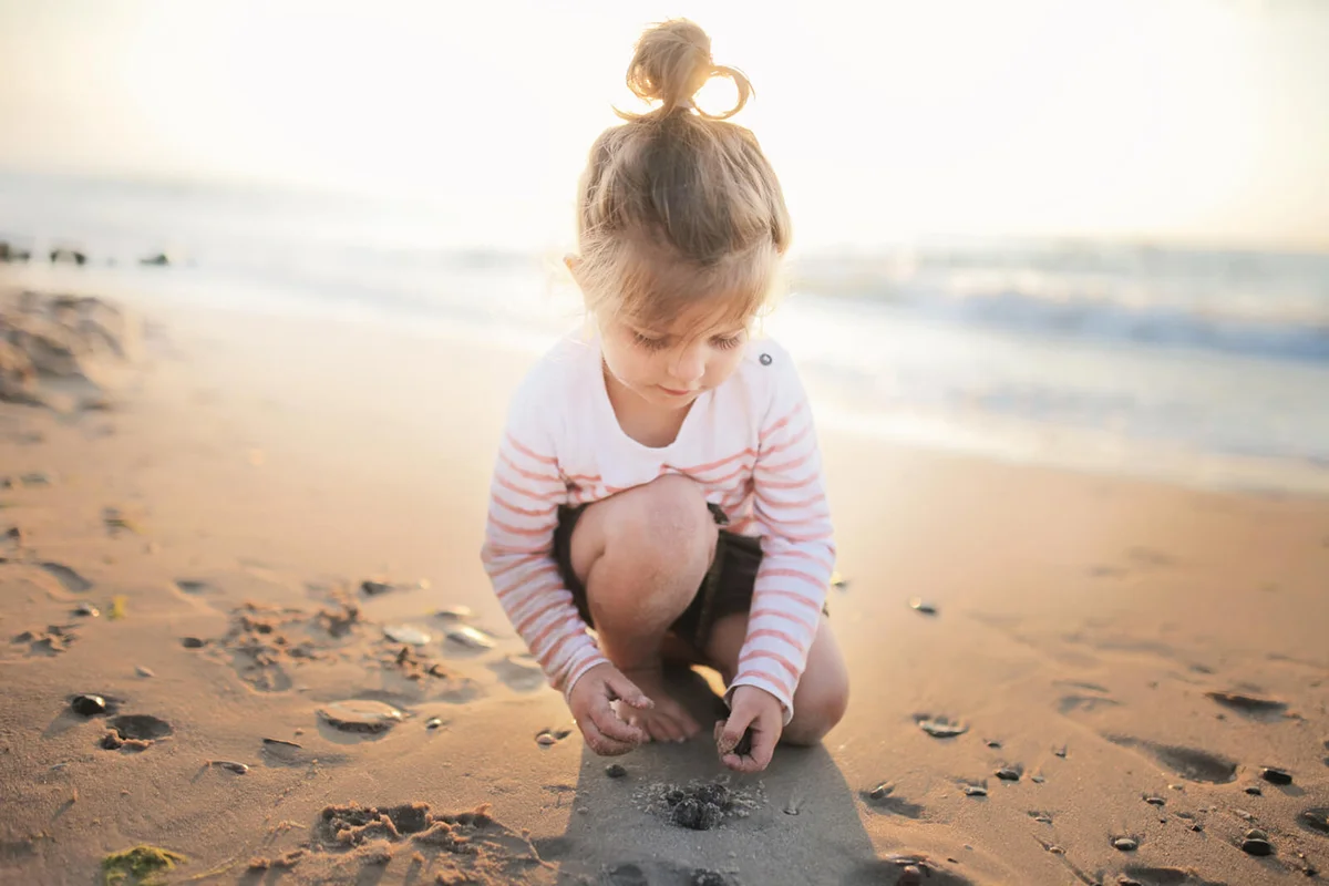 Small girl playing collecting stones on beach at sunset