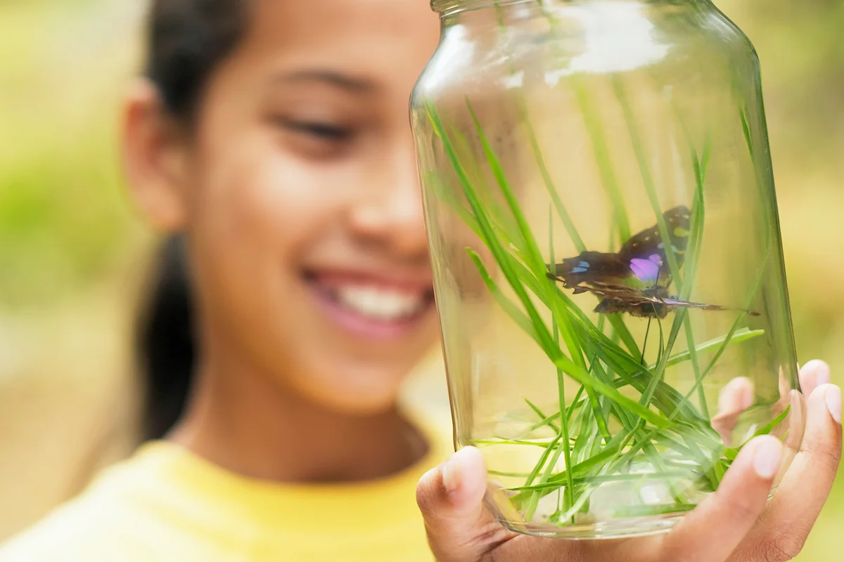 Girl looking at butterfly captured in jar