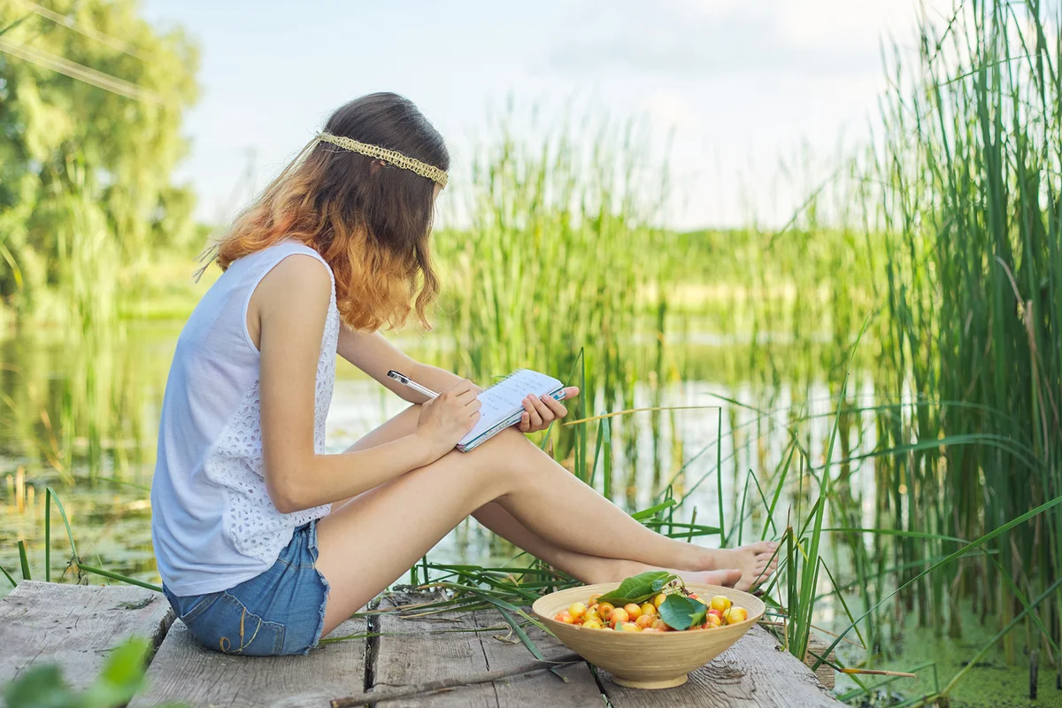 teenager sitting on bridge near water writing on a notebook