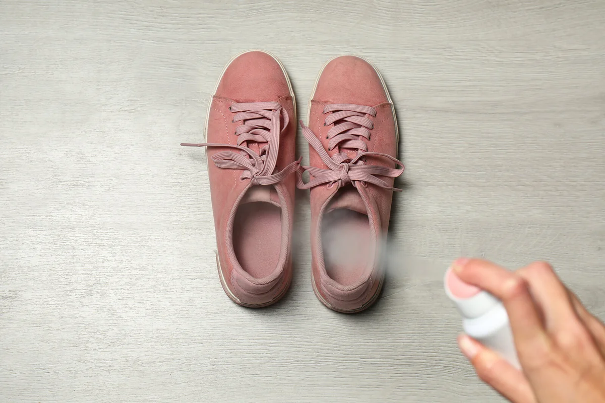 Woman spraying deodorant over pair of shoes at home