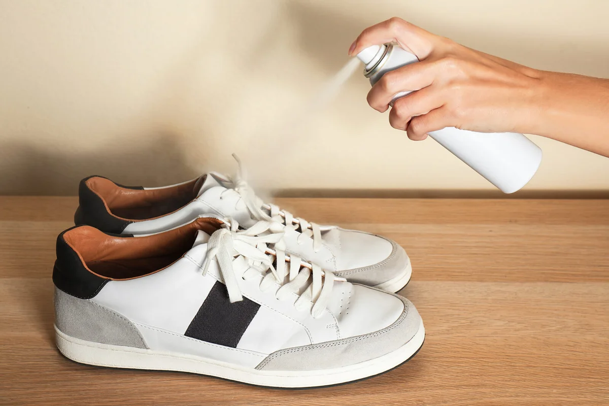 Woman spraying deodorant over pair of shoes at home