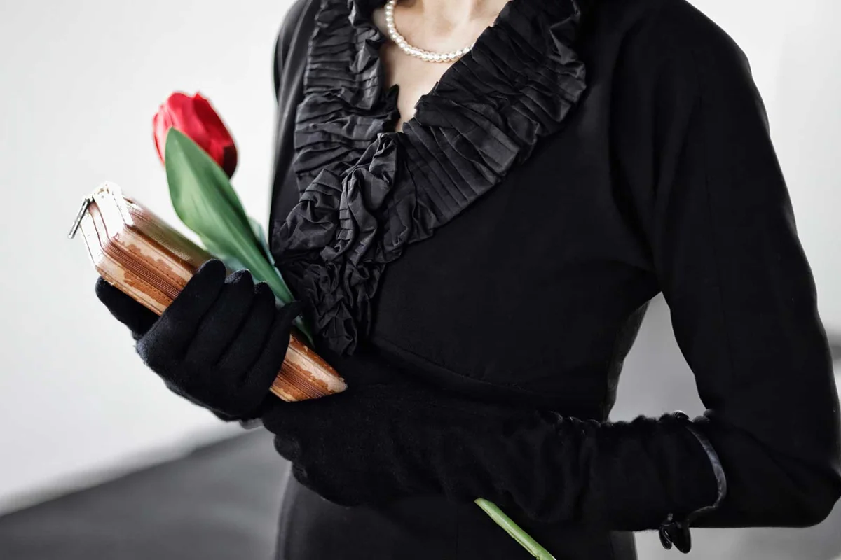 grieving woman in black dress holding a book and a flower