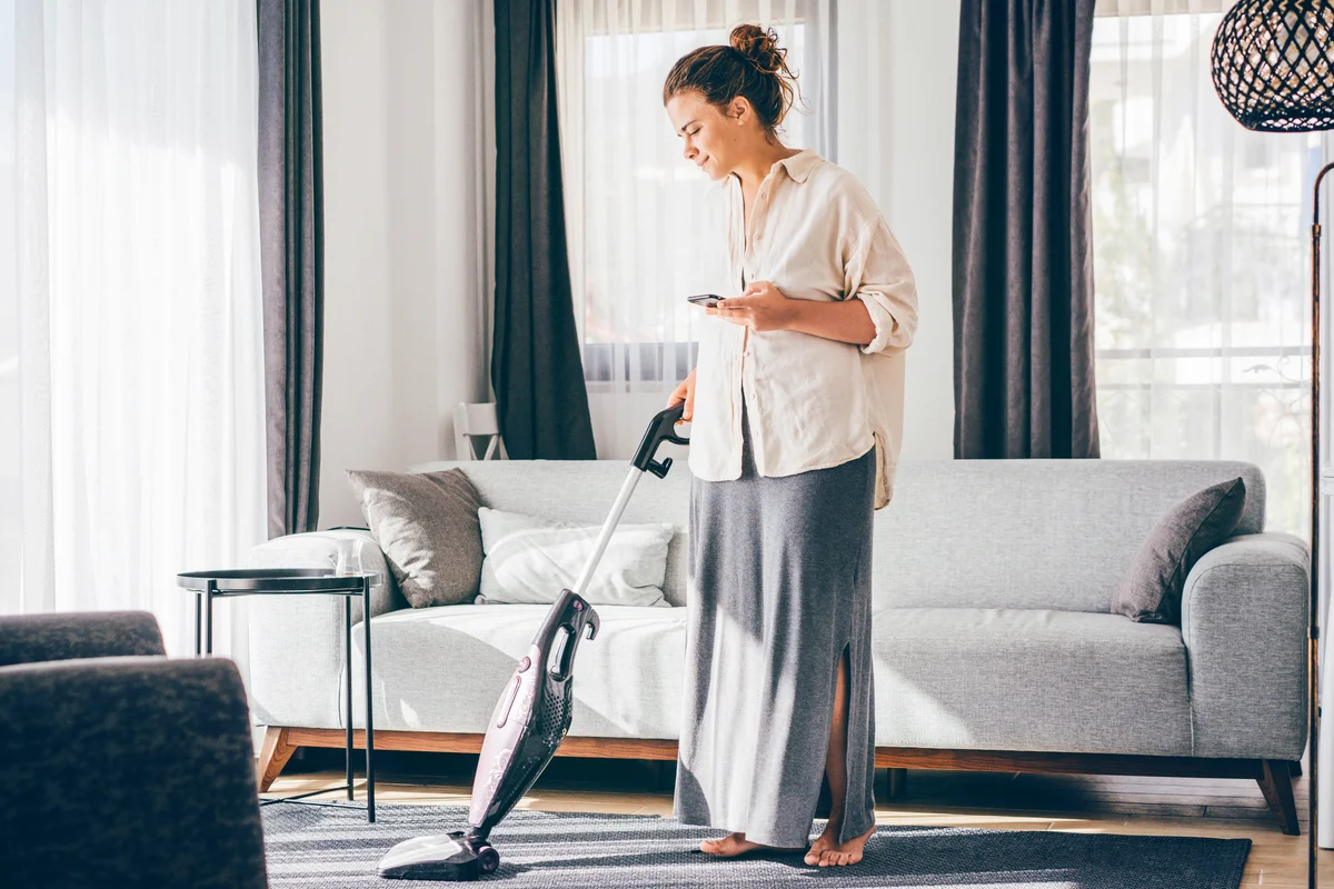 Woman talking on cell phone while vacuuming rug