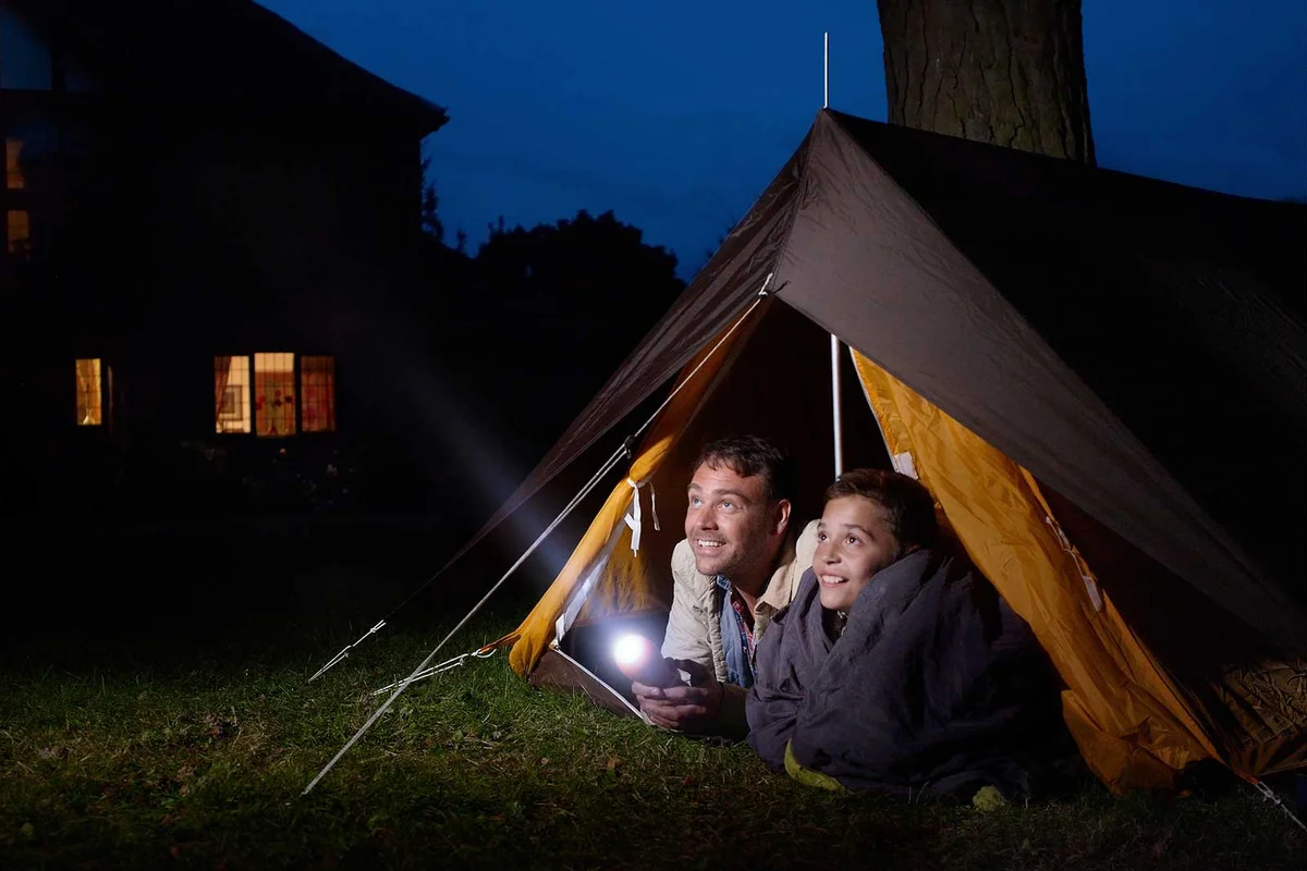 father and son stargazing in tent in backyard