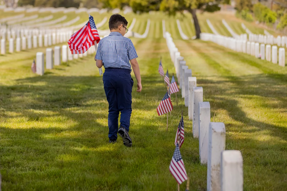 boy holding American flag walking through cemetery
