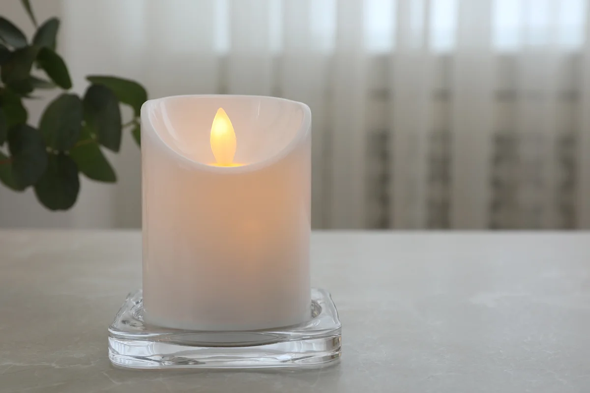 Glowing decorative LED candle on grey table