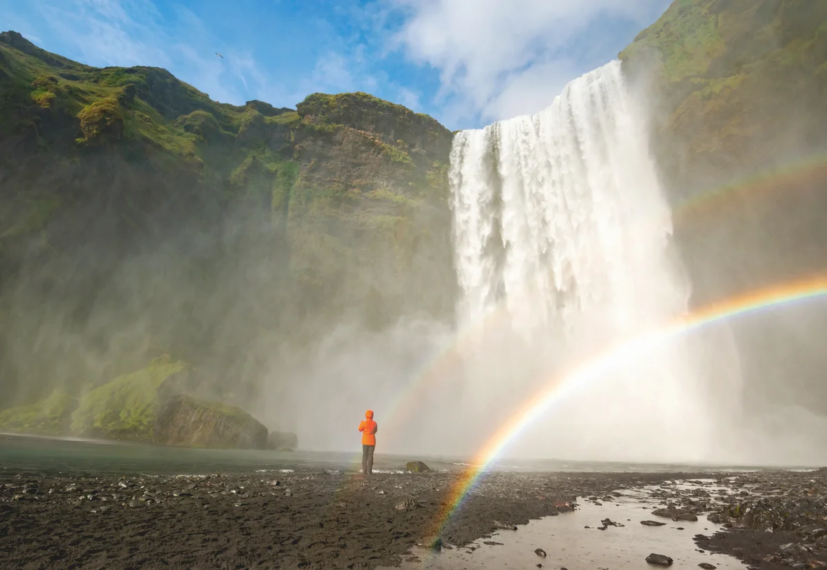 Man looking at waterfall in an idyllic landscape and double rainbow