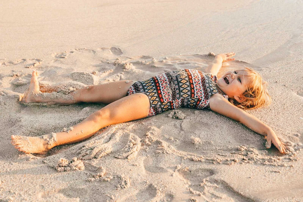 girl making sand angel at beach