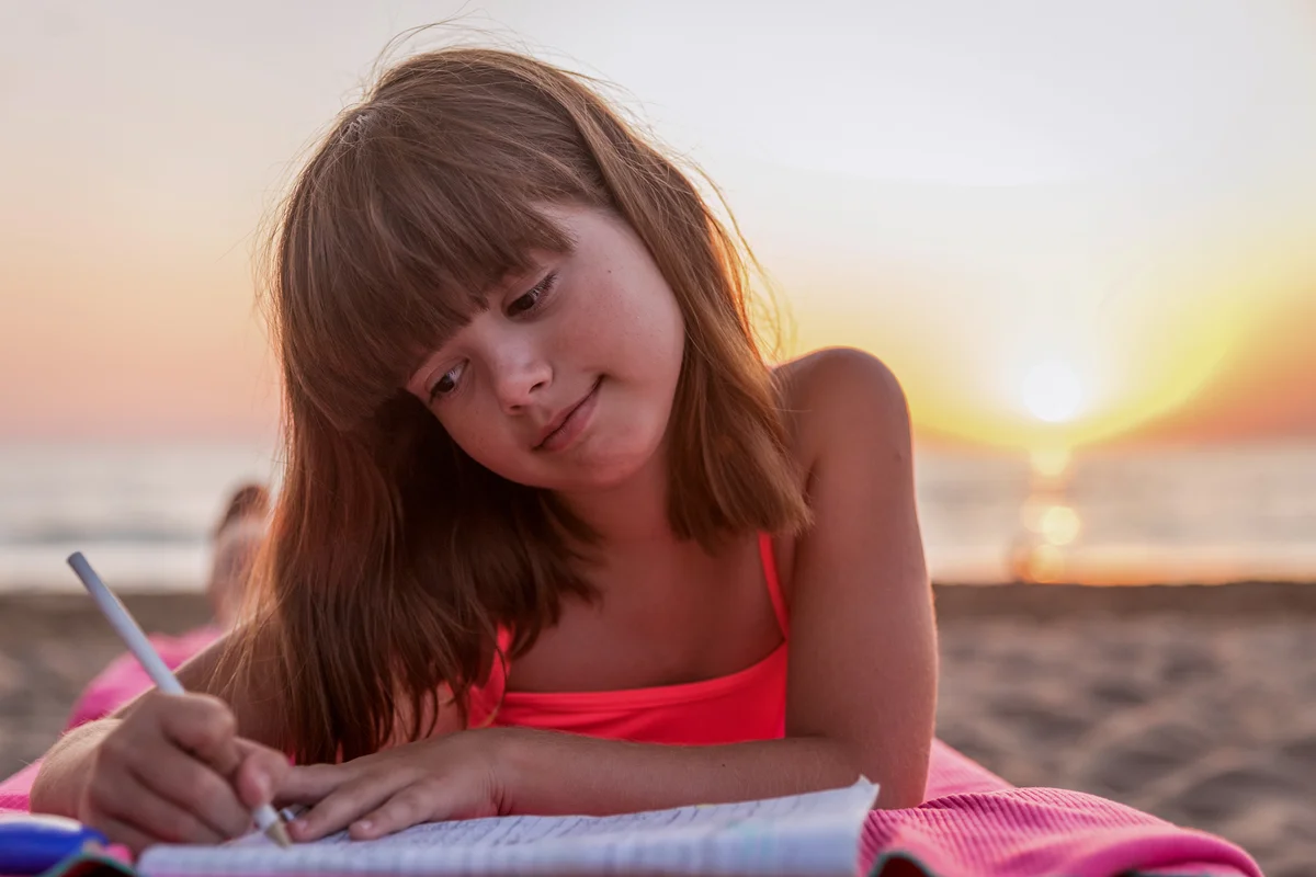girl writing in journal at beach