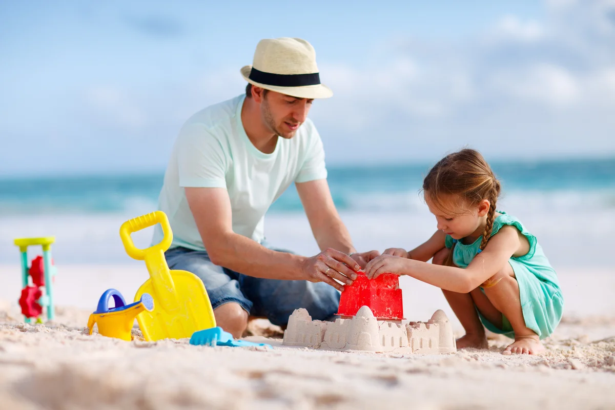 father and daughter building sand castle on beach