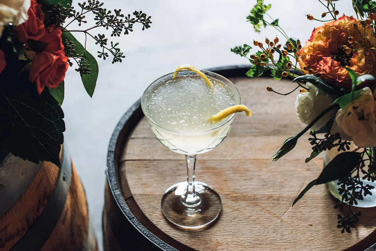 Ice Cold Cocktail In Champagne Coupe Glass Stemware With Lemon Zest Garnish On Whiskey Barrel