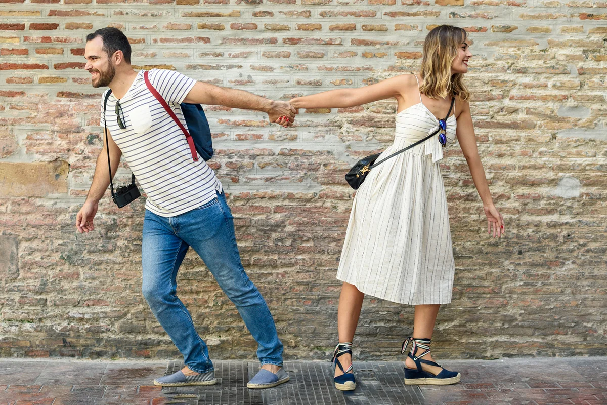 Couple holding hands walking in opposite directions at brick wall