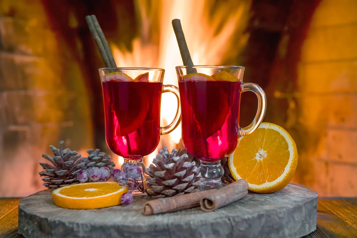 Two glasses of hot mulled wine with spices on wooden table against fireplace