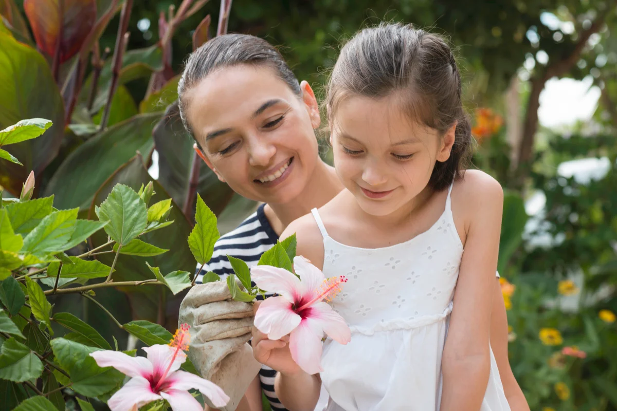 Mother and daughter in garden are looking at hibiscus flower