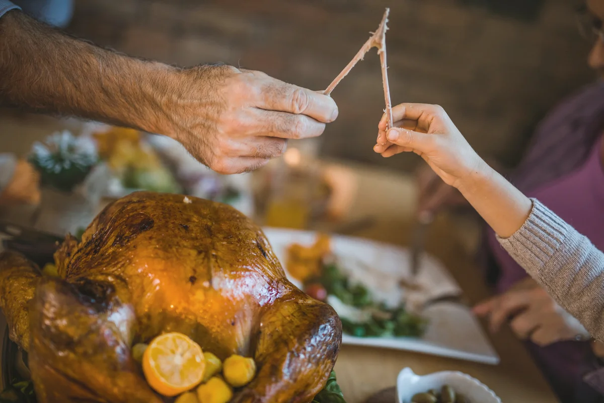 Unrecognizable man and child pulling wishbone on Thanksgiving dinner