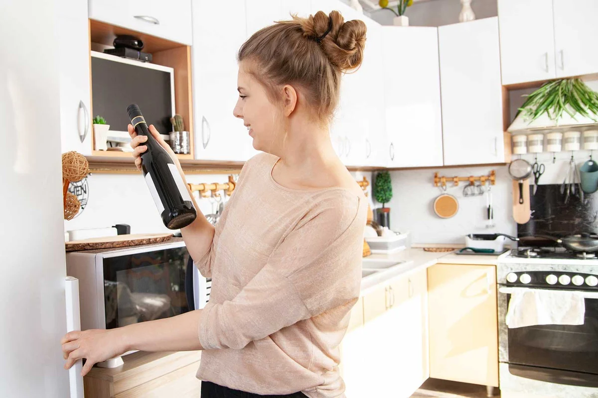 woman checking for expired wine in kitchen cabinet