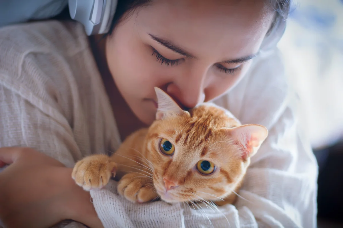 Woman holding and kissing orange cat