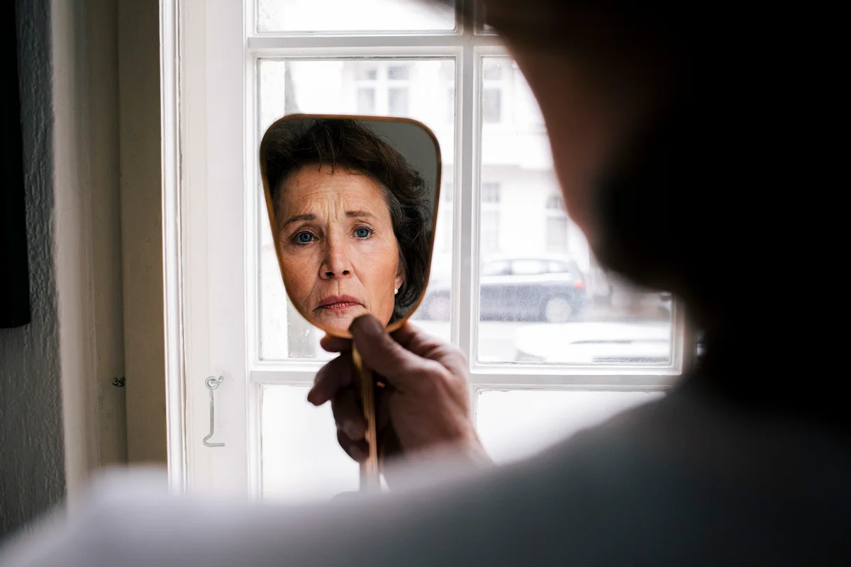 Reflection of worried woman on hand mirror at home
