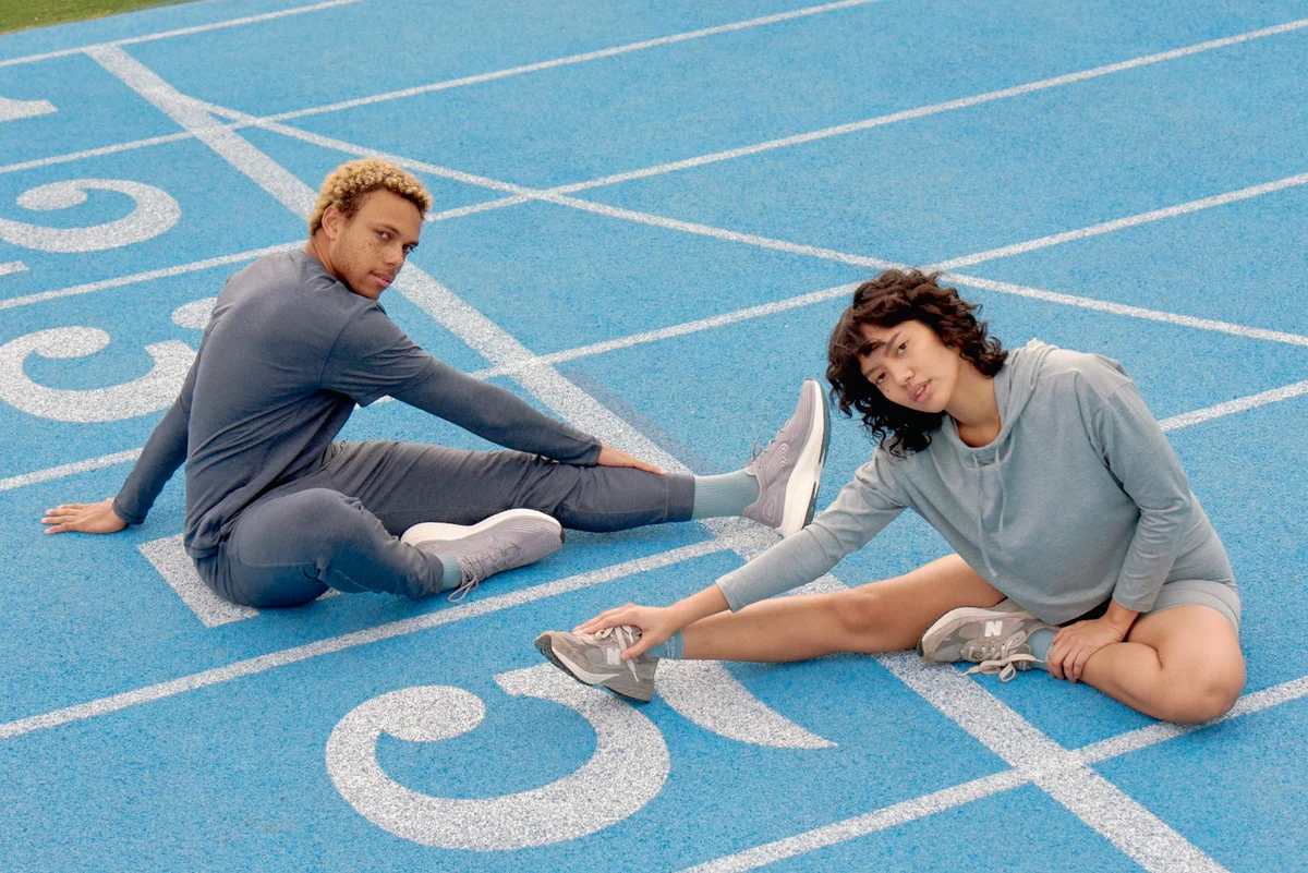 Photo of two models seated on the ground and stretching in Girlfriend Collective athleisurewear.