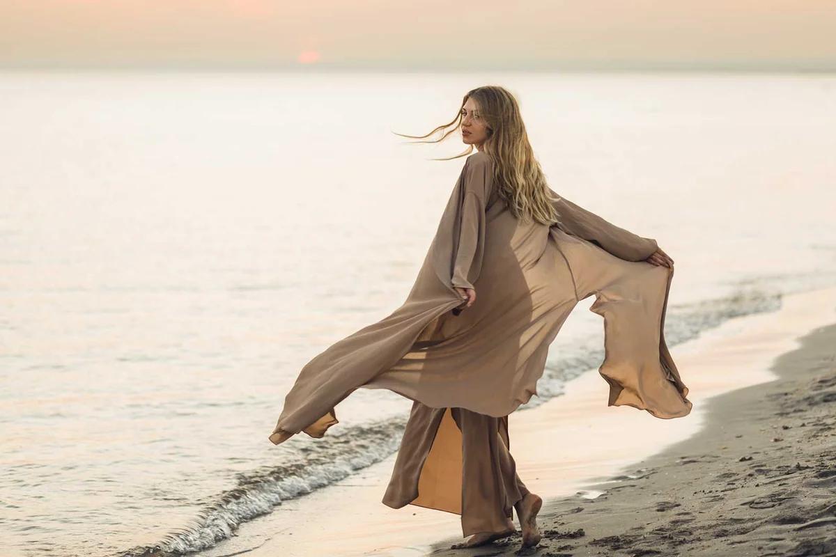 woman in flowing dress by ocean at sunset