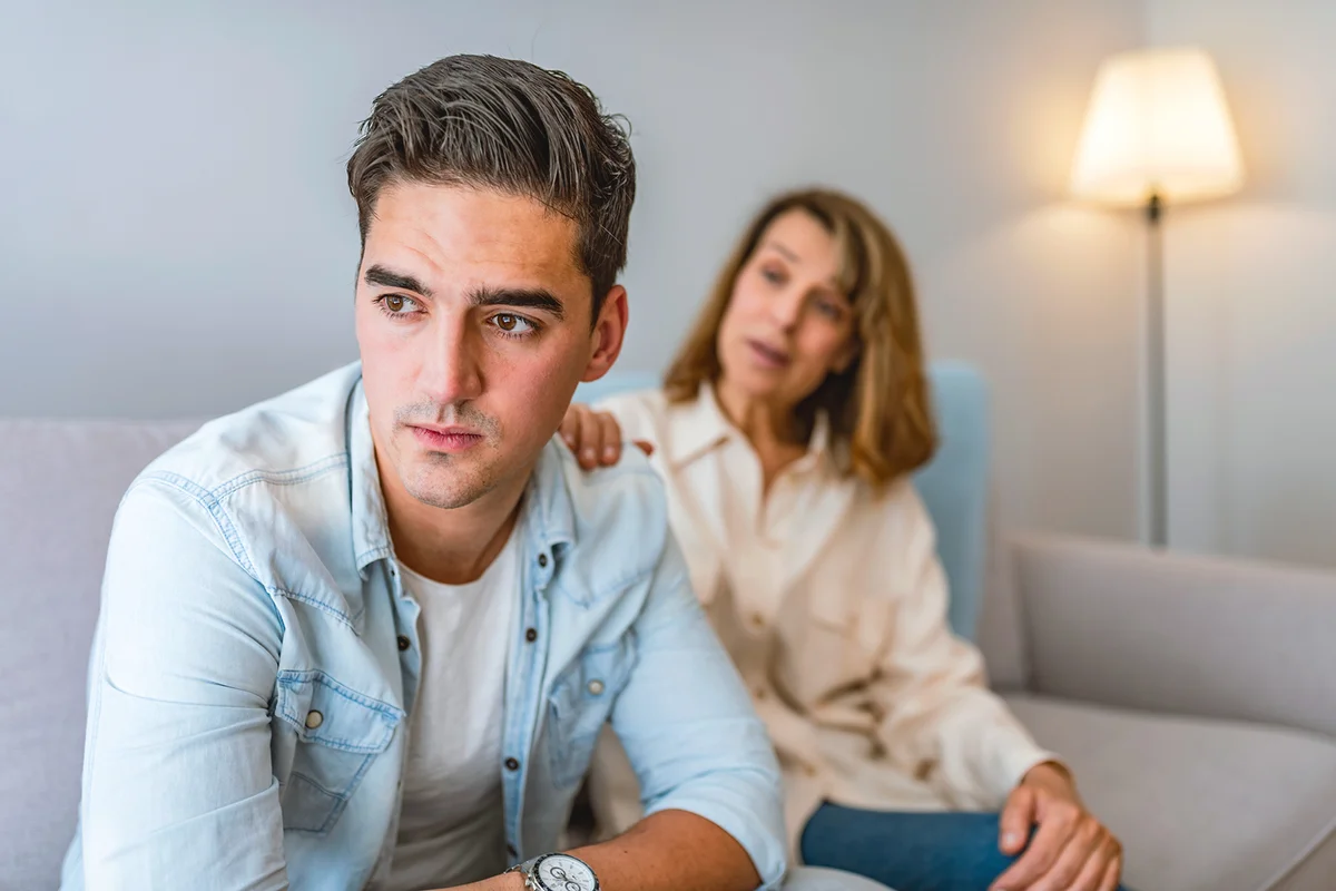 Frustrated mother talking to with her upset son sitting on the couch