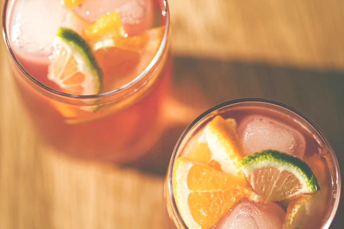 Top down view of 2 glasses of fruity punch with ice cubes and slices of lime and orange.