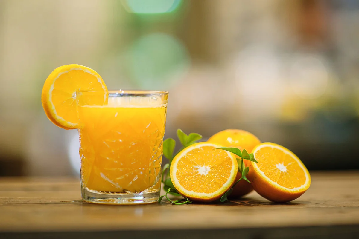 Fresh orange juice next to some orange slices on wooden table