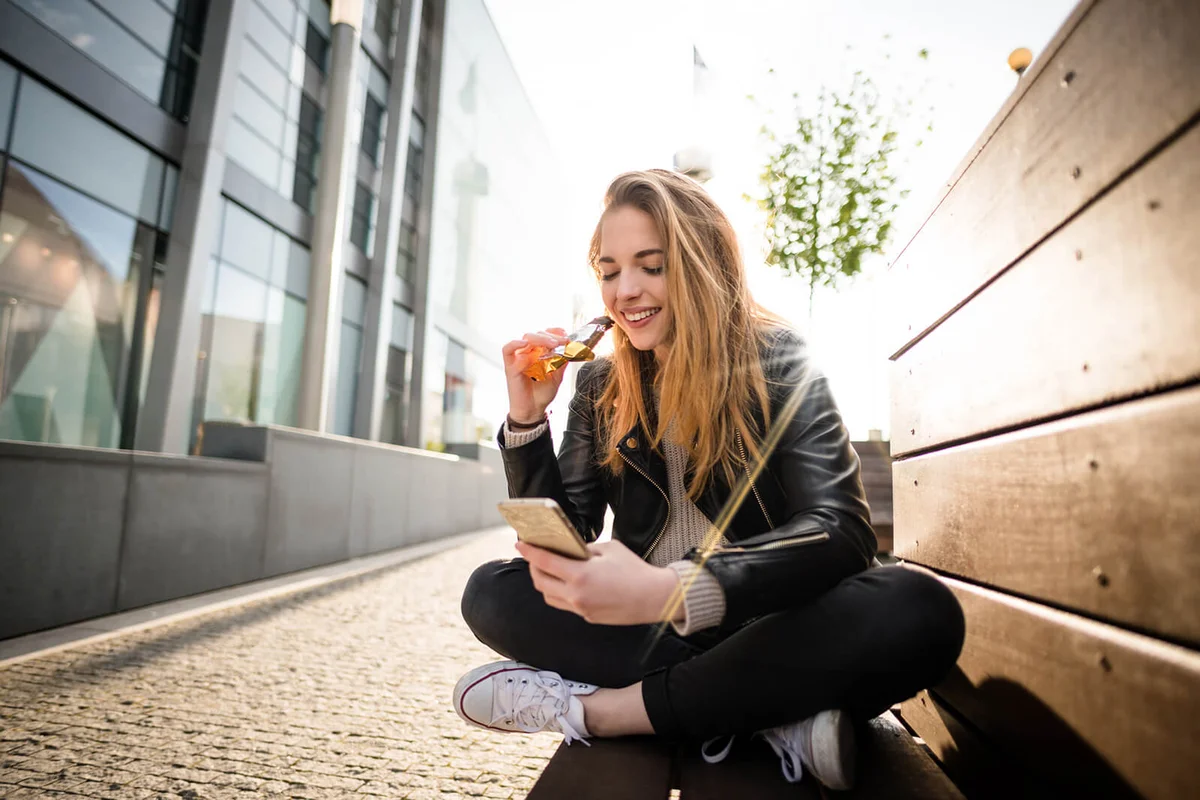 eenager eating chocolate on phone outddoor in street