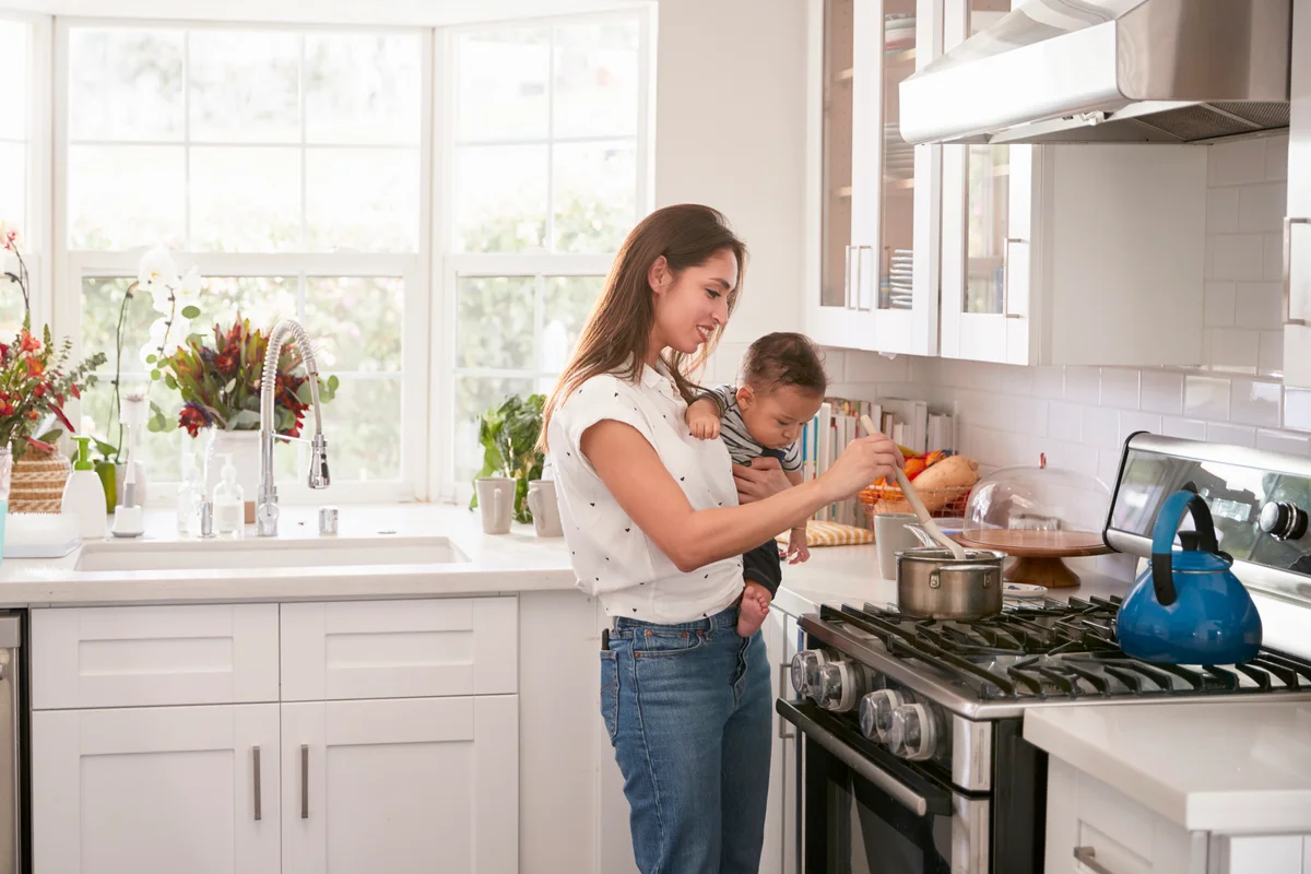 Multitasking mum holding her young baby while she makes food