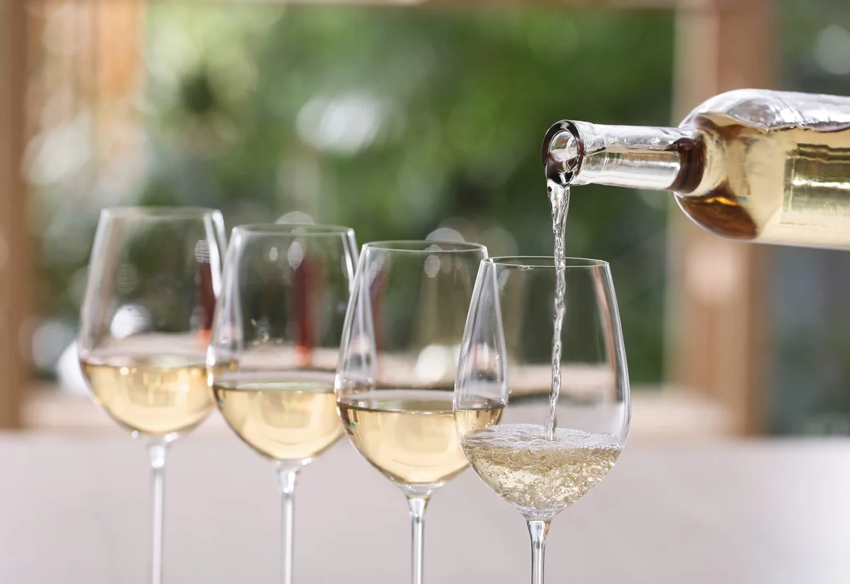 Pouring white wine from bottle into glass on blurred background