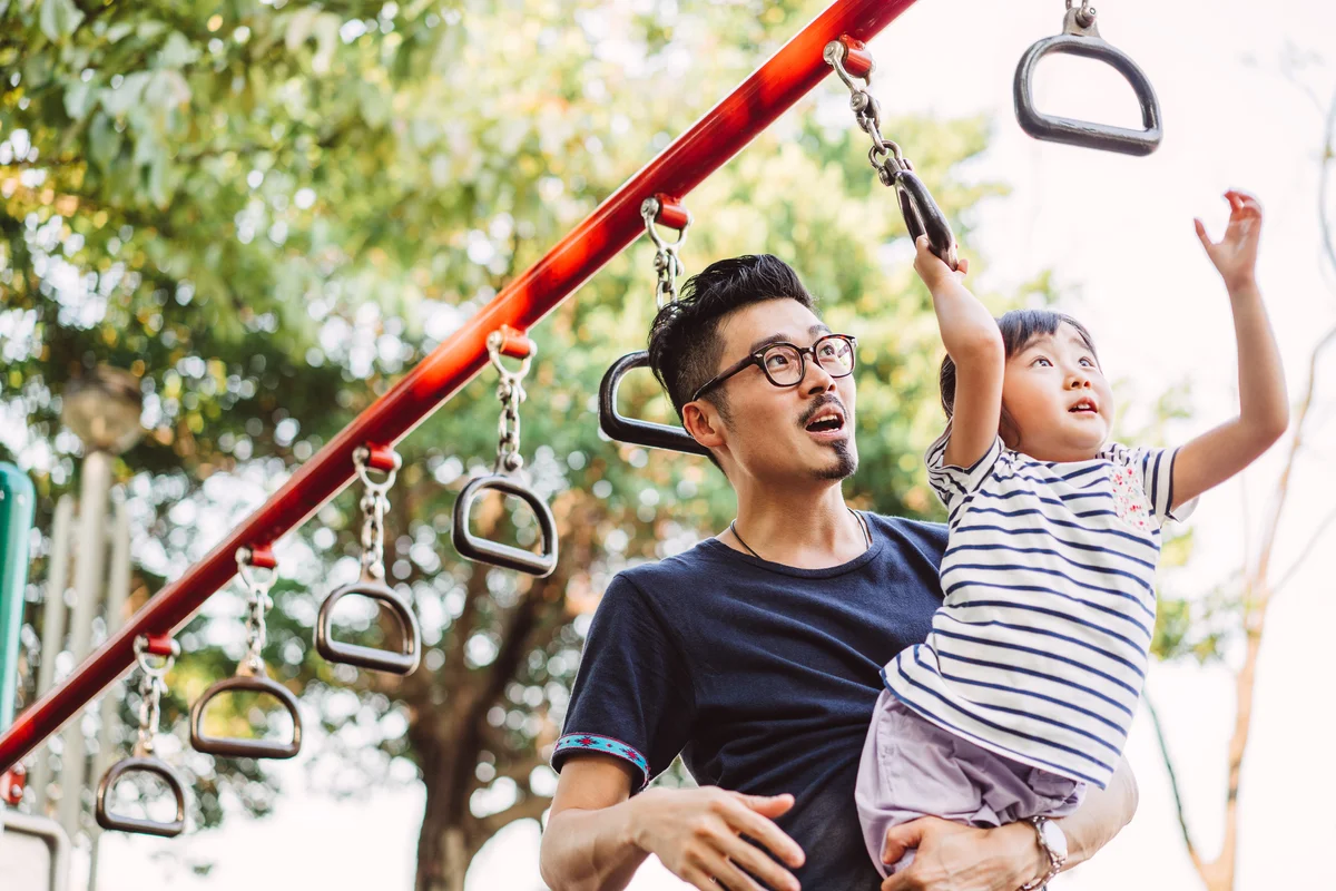 father helping daughter with playground monkey bars