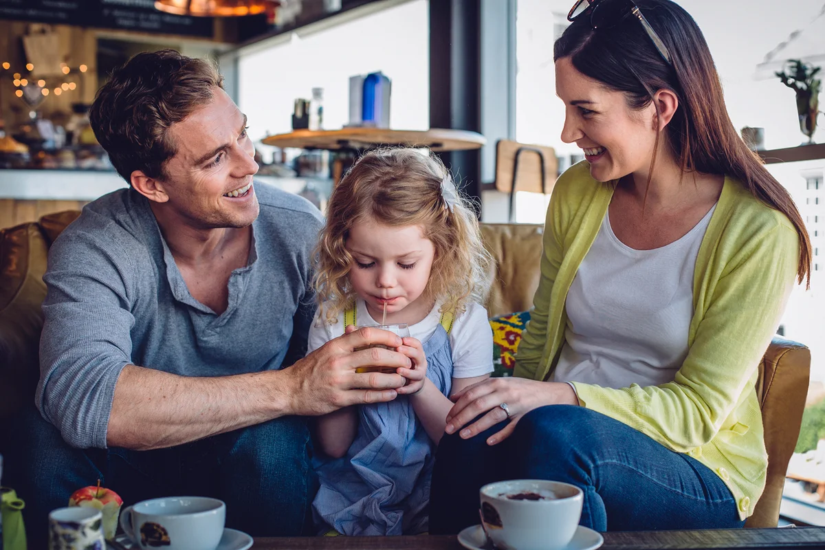 A couple with a little girl are sitting in a coffee shop enjoying a hot drink and refreshments