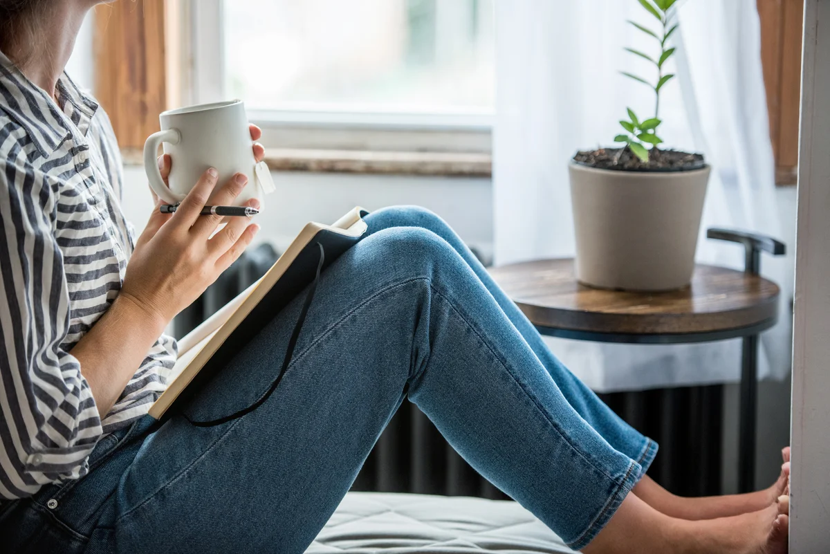 Young woman takes a break to write in her journal and drinks tea