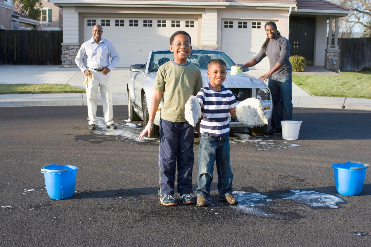 Boys playing with sponges while their family washes the car