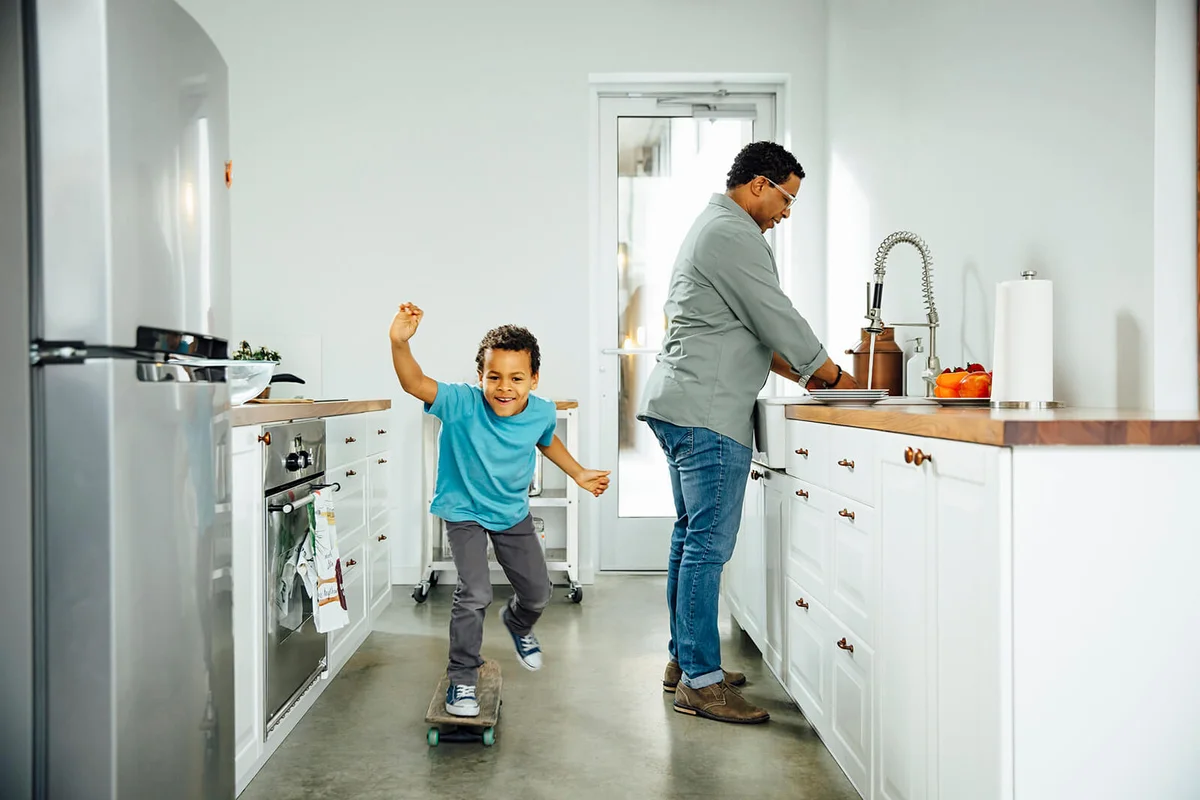 Boy skateboarding near father in kitchen