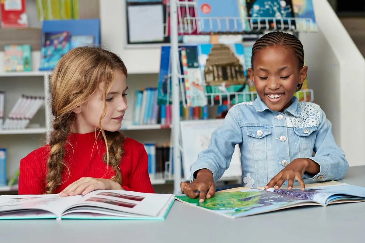 two school children reading books in library