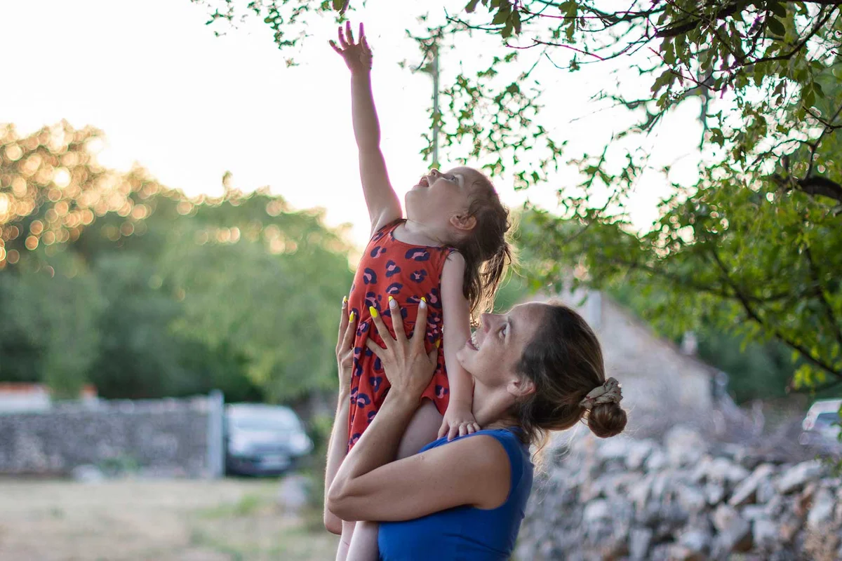 mother helping daughter reach branch of tree