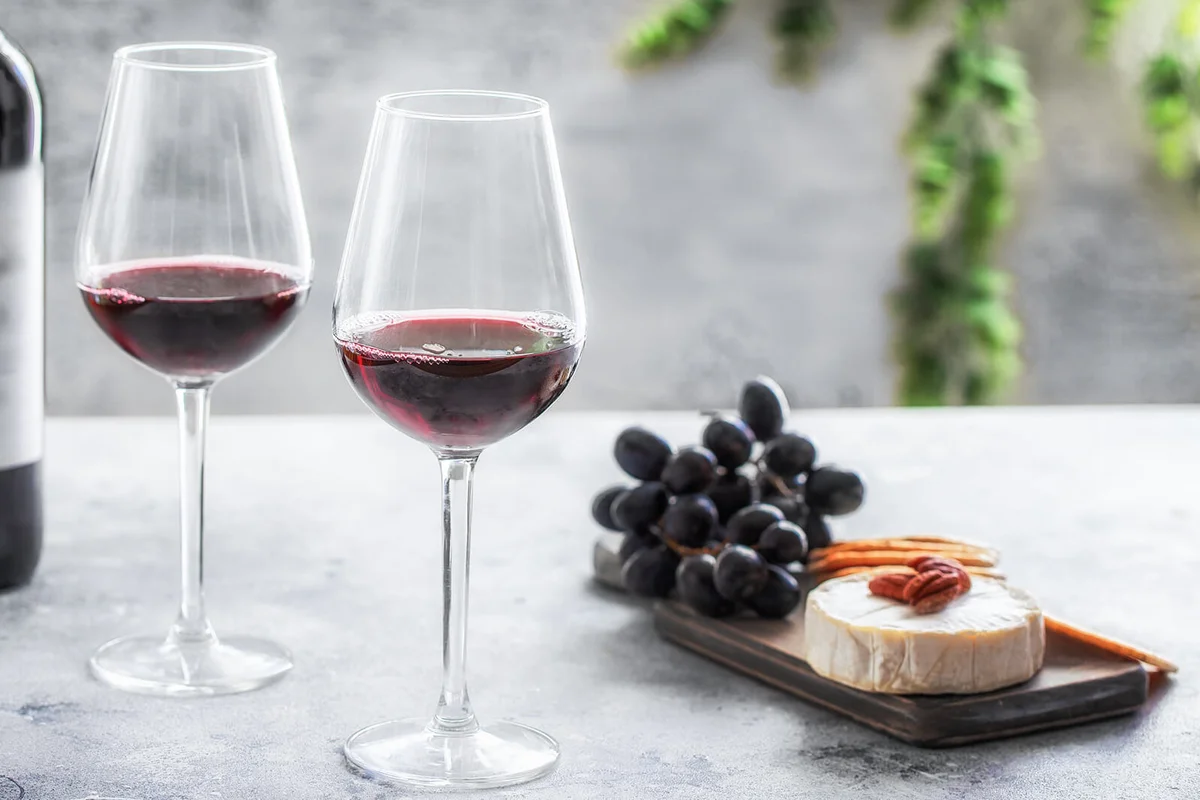 Red wine bottle with two glasses and cutting board with different snacks