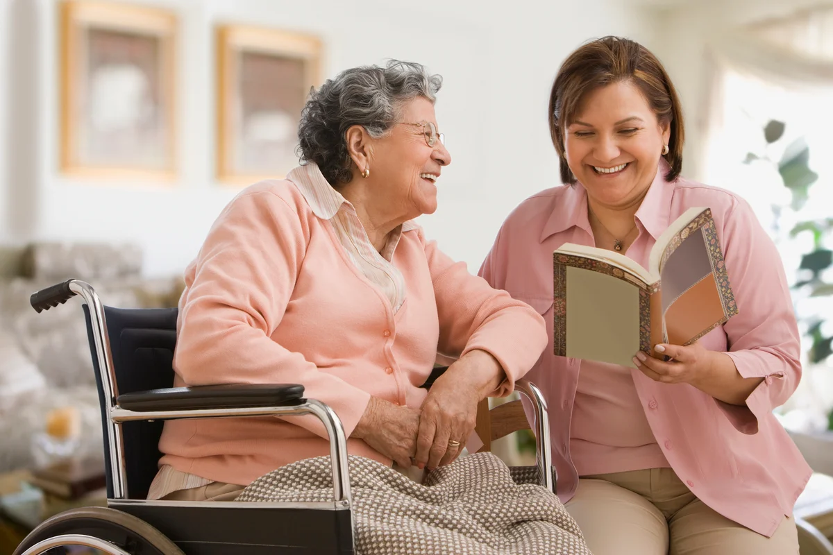 caregiver reading to elderly woman in wheelchair
