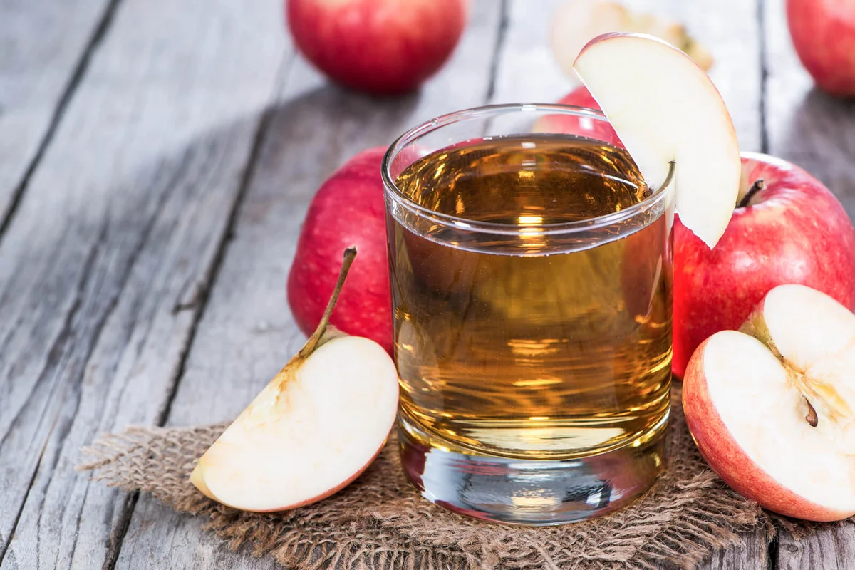 Glass of apple cider surrounded by freshly-cut apples