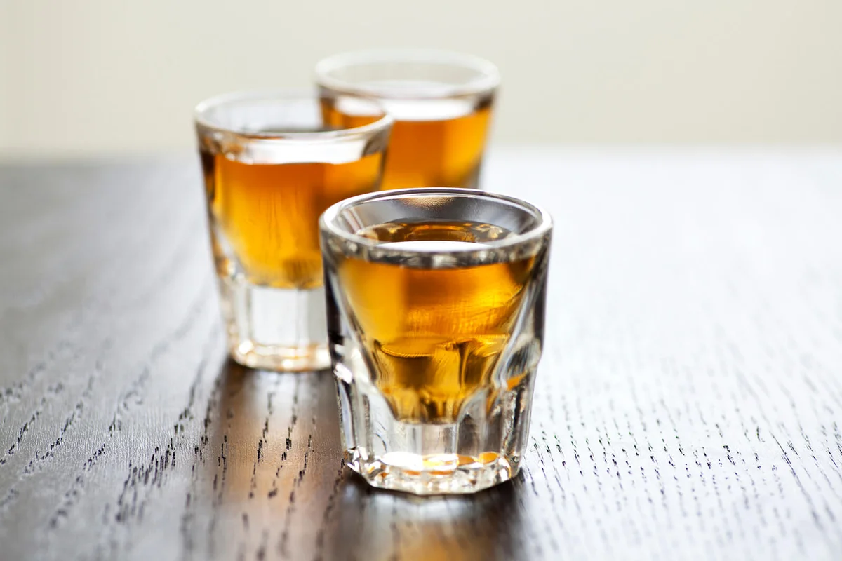 Three shot glasses full of dark colored alcohol on top of a bar table