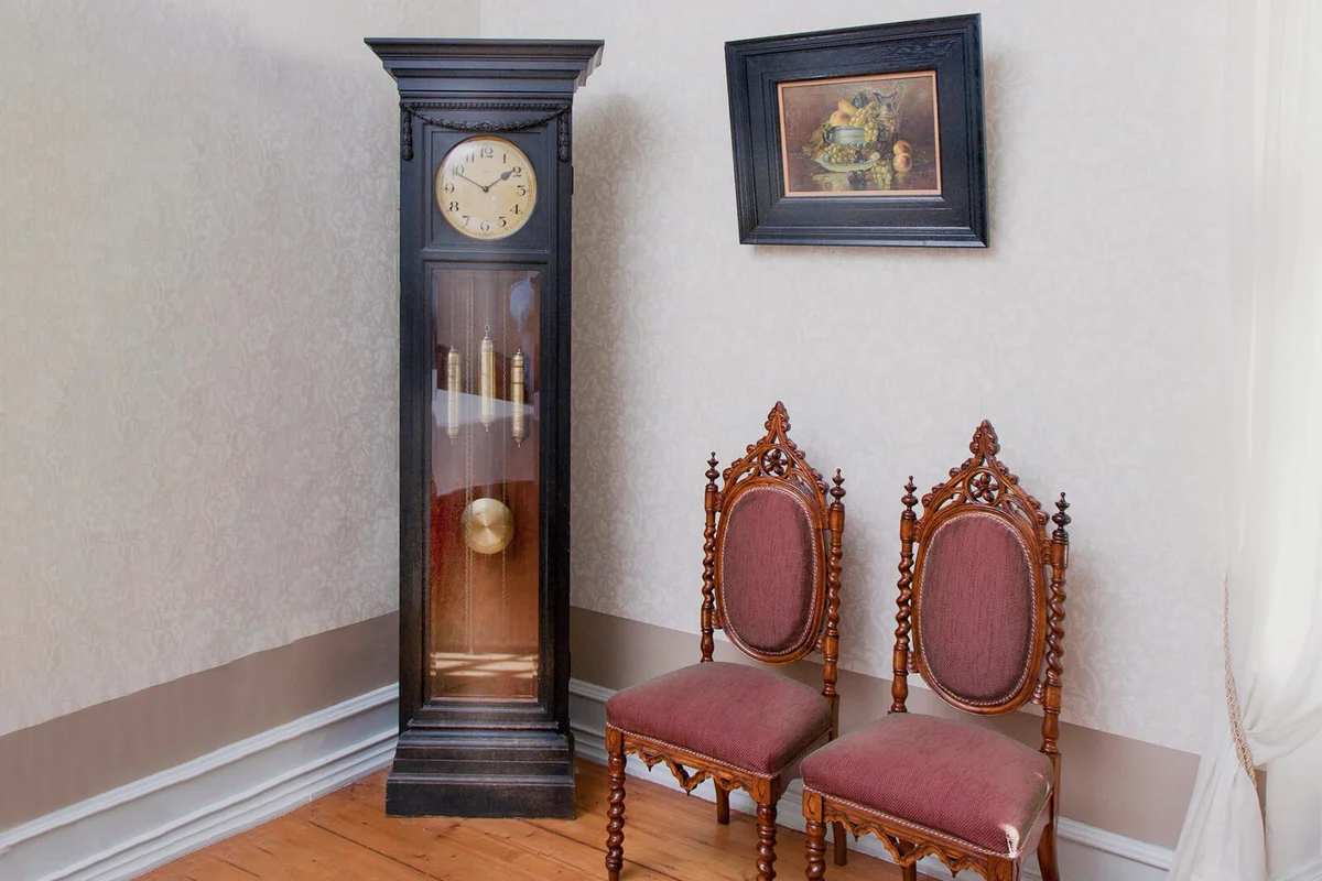 A grandfather clock and two chairs in a room in a hotel