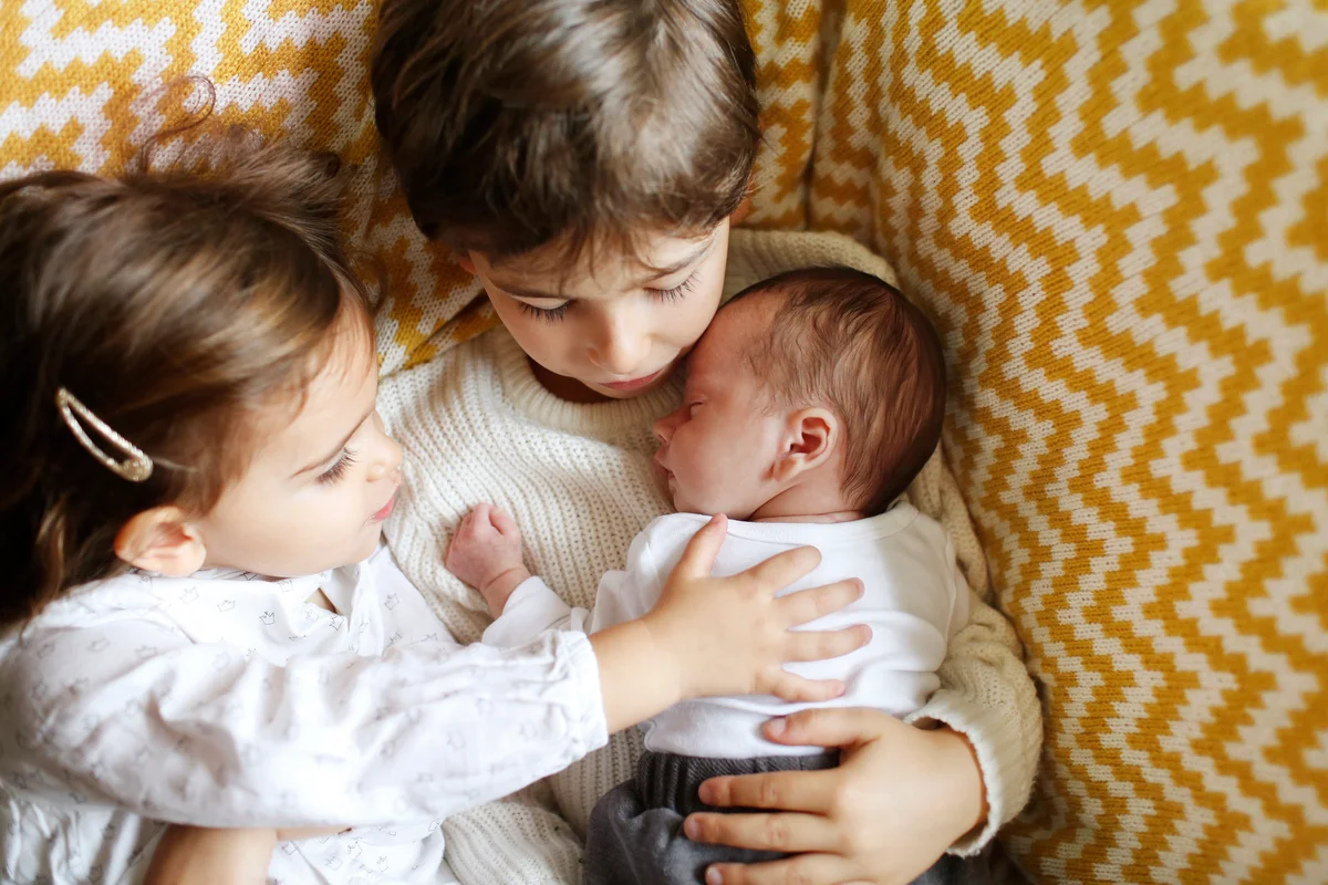 siblings cuddling newborn brother