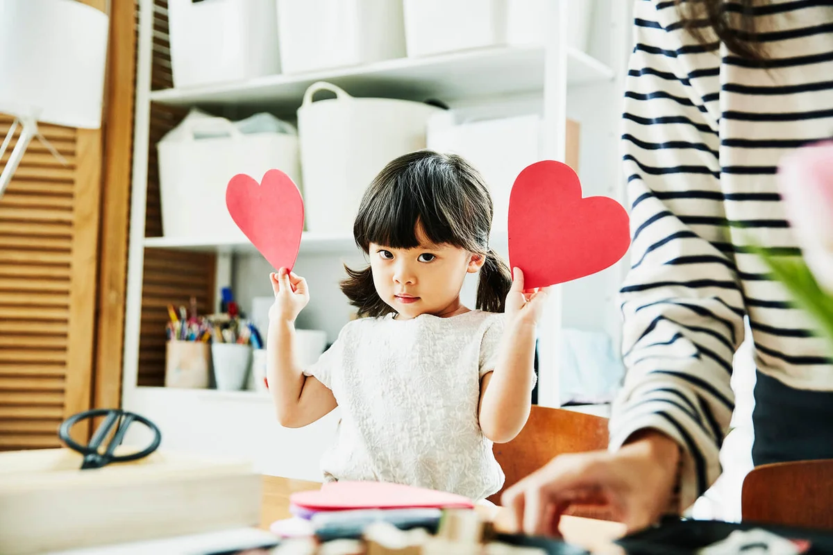 Young girl showing paper hearts while making Valentines Day cards in home
